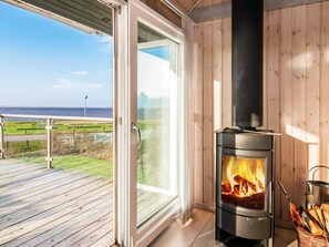 A modern room with a wood-burning stove, a glass door leading to a deck, and a view of the sea.