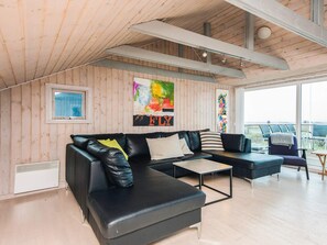 En moderne stue med en sort lædersofa, et lille sofabord og udsigt til naturen gennem store vinduer.