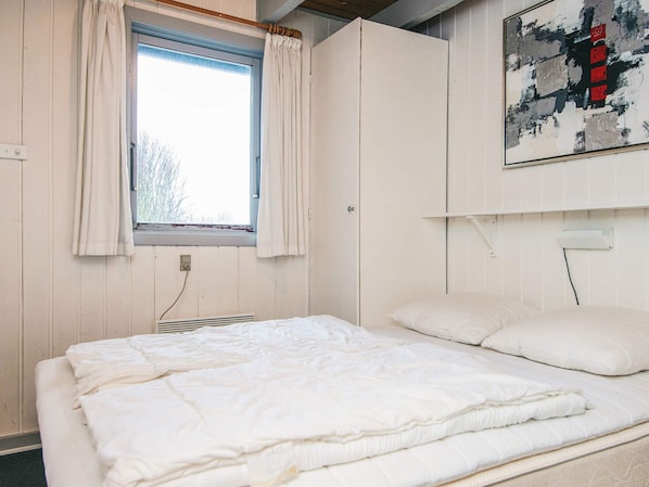 A room with a bed, a window with curtains, a wall-mounted air conditioner, and a painting.