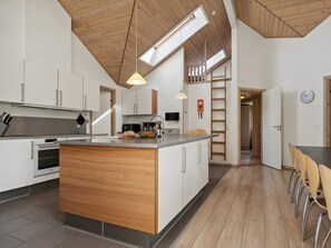 A modern kitchen with a central island, wooden ceiling, and built-in appliances.