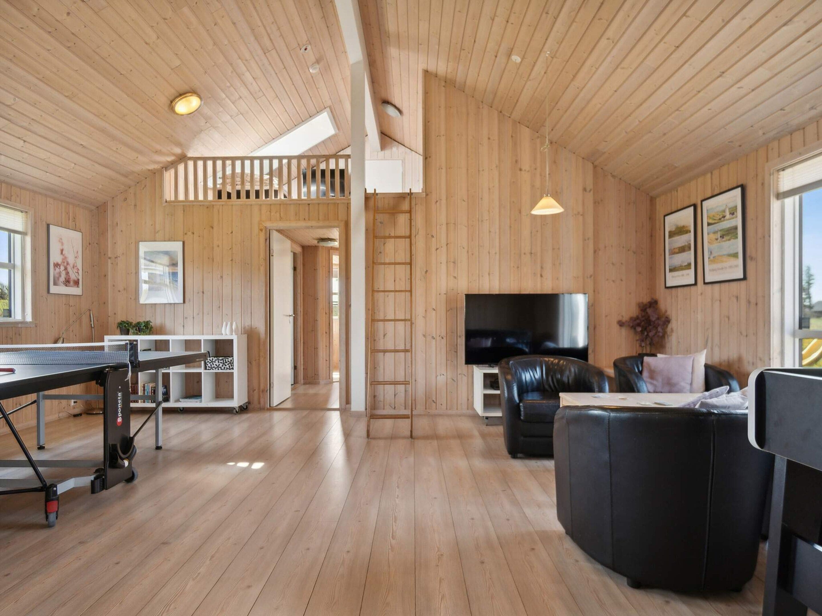 A spacious living area with a wooden floor, a TV, a sofa, and a ping pong table.