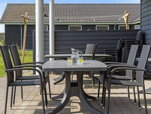En udendørs terrasse med et bord, stole, en kande og glas.