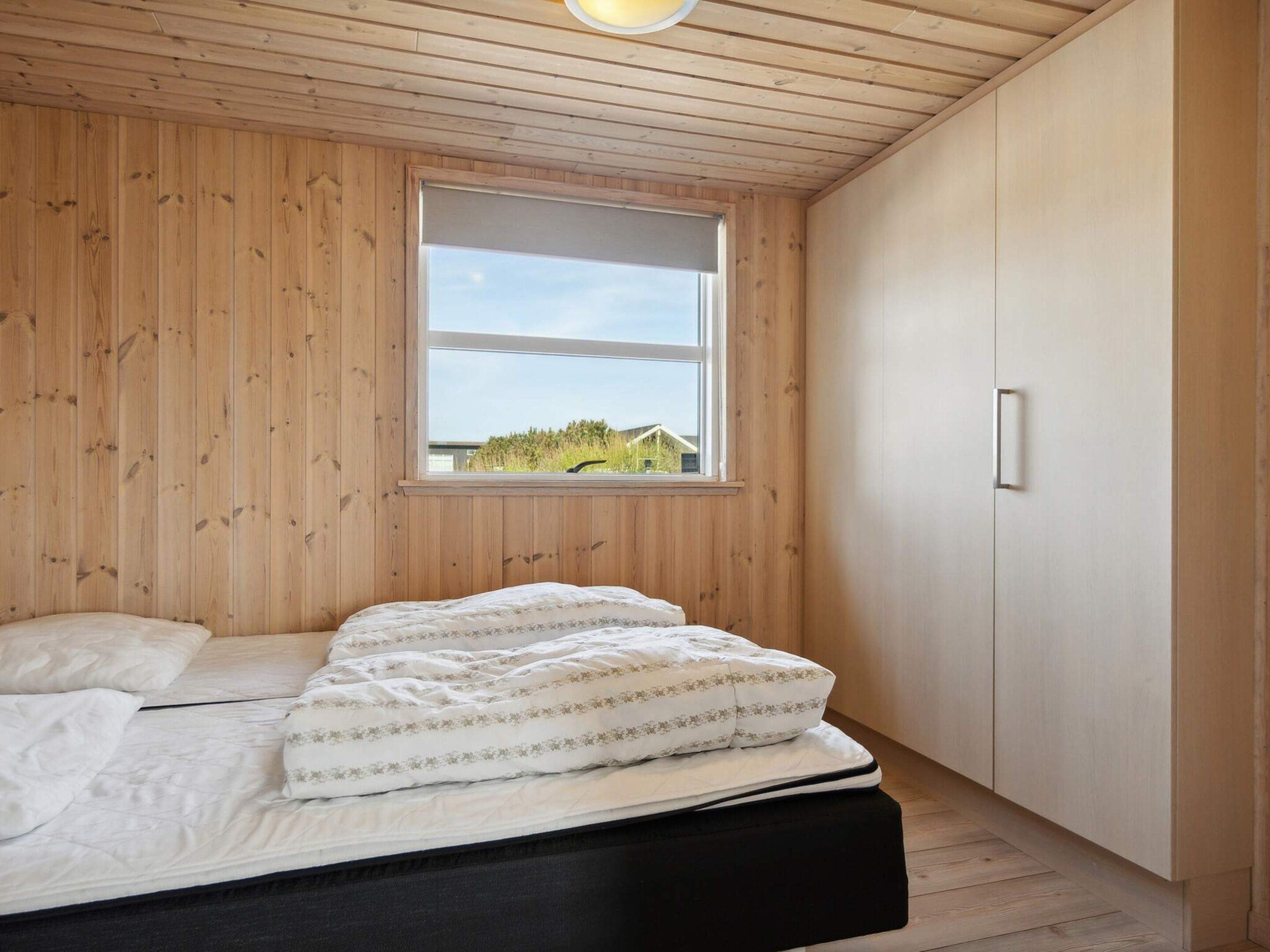 Un dormitorio con techo de madera, una ventana con vistas, una cama con ropa de cama blanca y un armario.