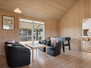 A spacious room with wooden walls and ceiling, a leather sofa, a table, and a foosball table.