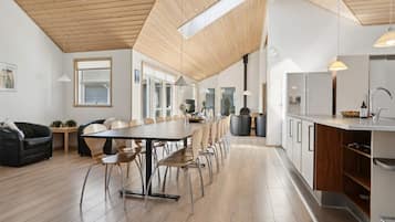 A modern kitchen with a long island, wooden flooring, and a high ceiling with skylights.