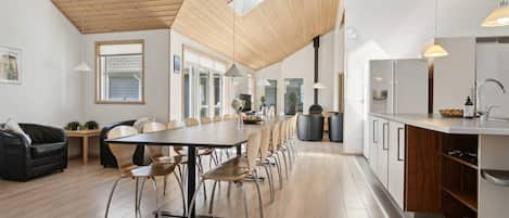 A modern kitchen with a long island, wooden flooring, and a high ceiling with skylights.
