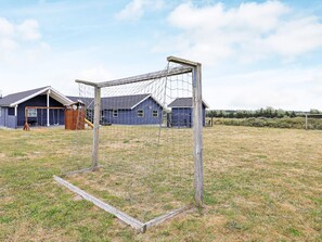 A fenced soccer goal in a grassy field with a blue building in the background.