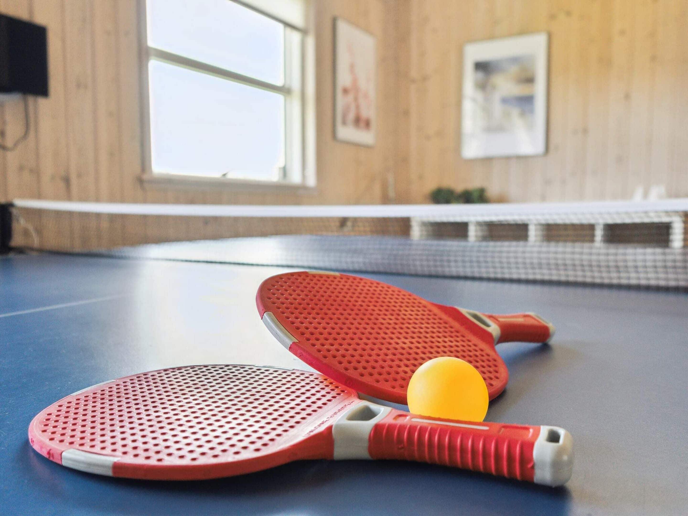 A ping pong table with two red paddles and a yellow ball.