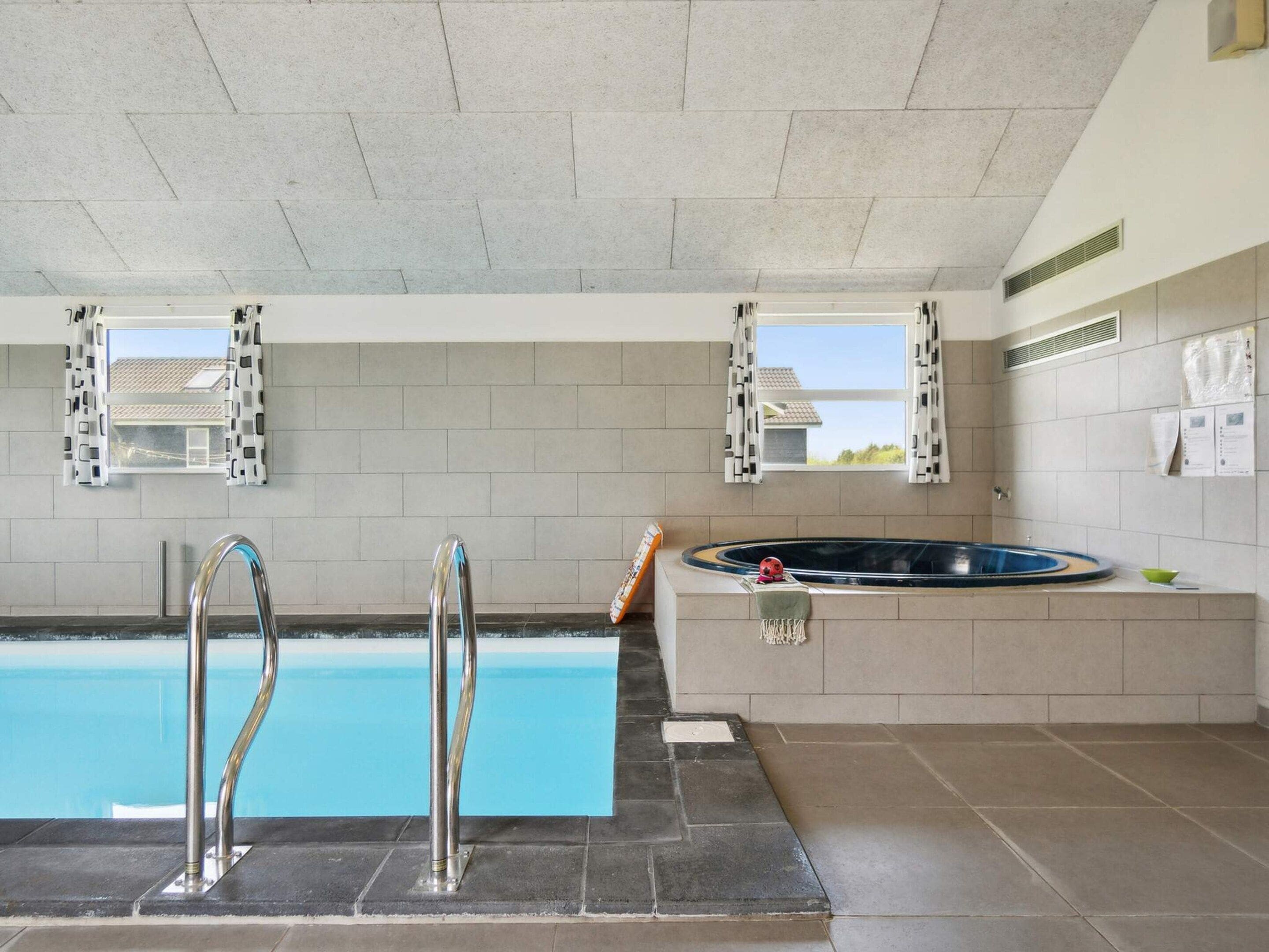 A swimming pool with two metal ladders, a hot tub, and two windows with shutters.
