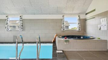 En swimmingpool med to metalstiger, et boblebad og to vinduer med persienner.