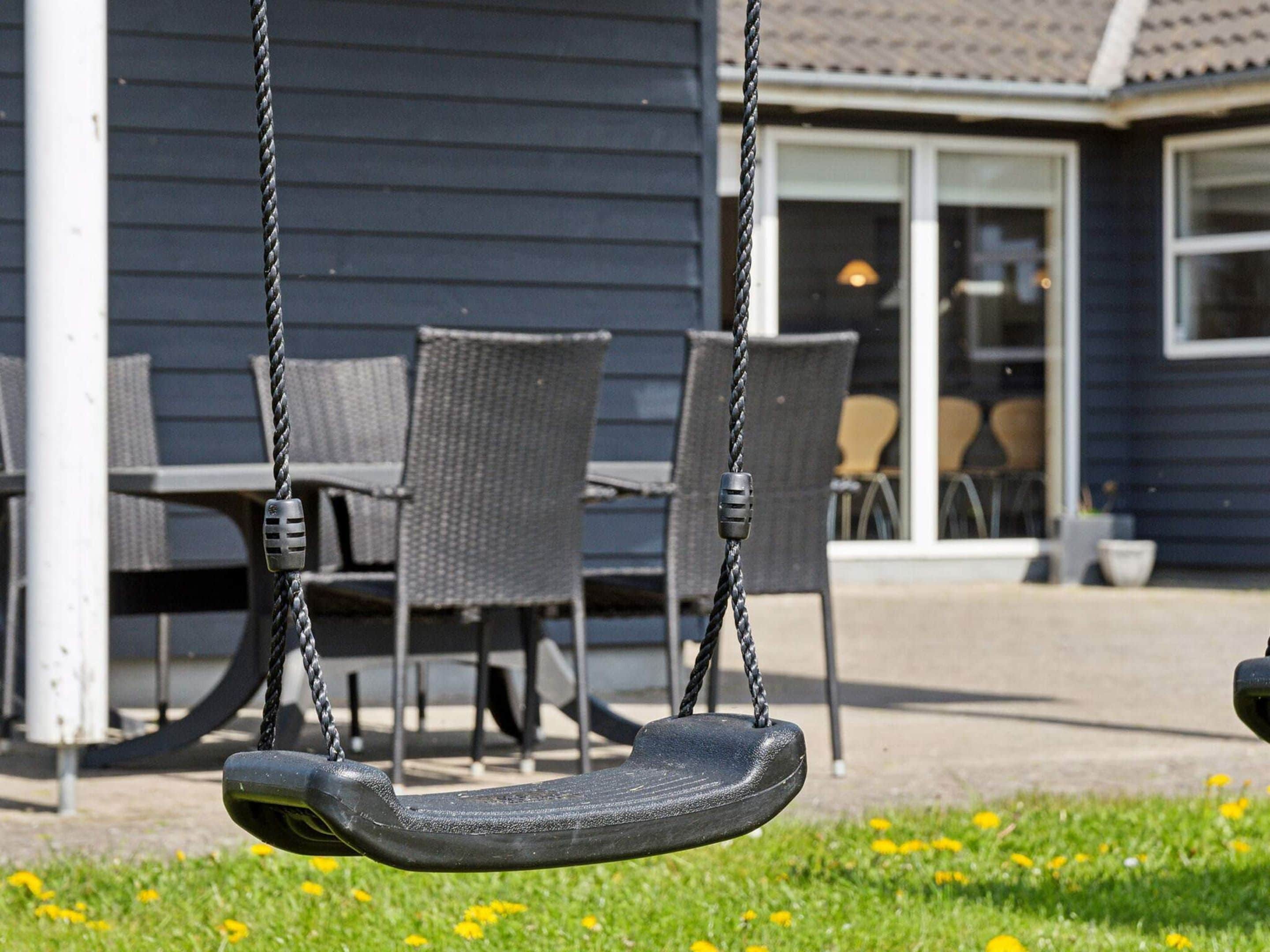 A swing set with a metal frame and black seat, positioned in front of a house with a porch and dining area.