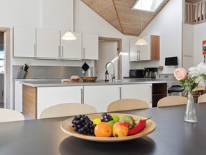 Et moderne køkken med hvide skabe, et rustfrit stål køleskab og et spiseområde med et bord dækket til to personer.