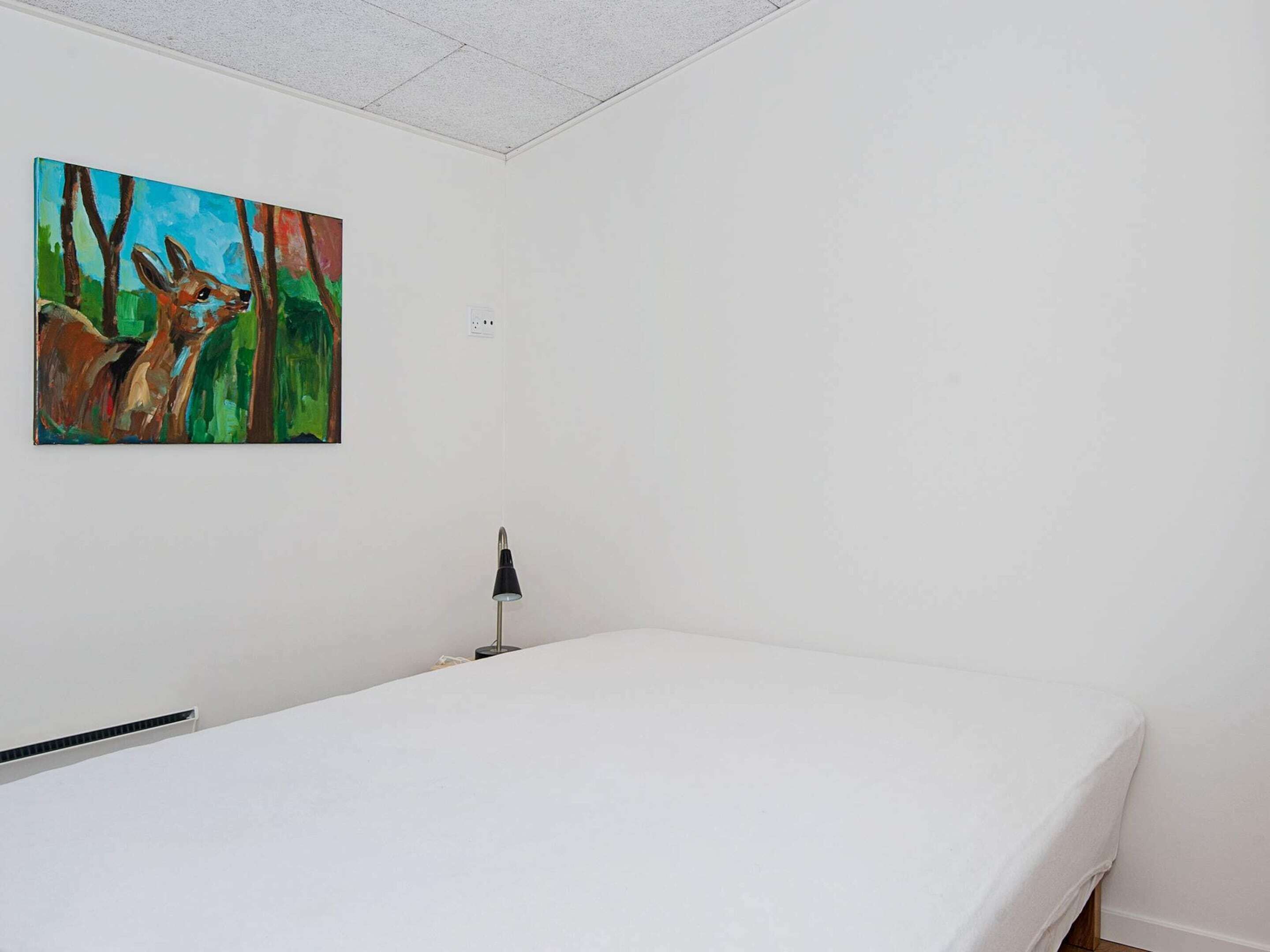 A room with a bed, a painting of a deer, and a lamp.