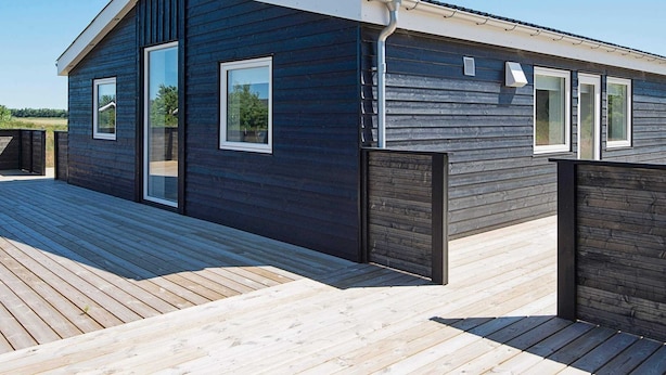 A modern building with a dark exterior, large windows, and a wooden deck.