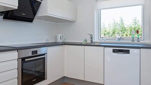 A modern kitchen with white cabinets, a Bosch oven, a dishwasher, and a window with a view of greenery.