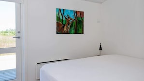A bedroom with a bed, a door, a painting on the wall, and a lamp.