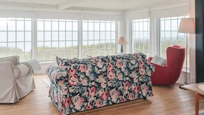 A room with a floral-patterned sofa, a red armchair, and a view through large windows. - 5 Person Holiday Home in Juelsminde (Juelsminde)