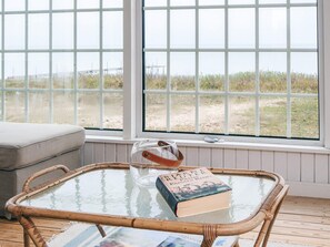 Ein Zimmer mit Glastisch, einem Buch und einem Korbstuhl.
