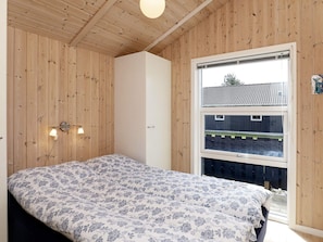 A bedroom with a bed, wooden walls, a window, and a light fixture.