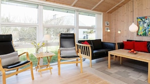A modern living room with wooden flooring, large windows, a black leather sofa, wooden chairs, and a dining table. - 4 Star Holiday Home in Thisted (Thisted)