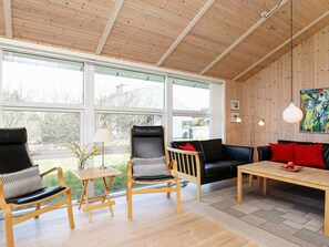 Een moderne woonkamer met houten vloeren, grote ramen, een zwarte leren bank, houten stoelen en een eettafel.