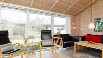 A modern living room with a wooden ceiling, large windows, and a black leather sofa.