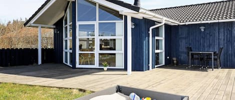 A modern house with a large glass door, a deck, and a sandpit.