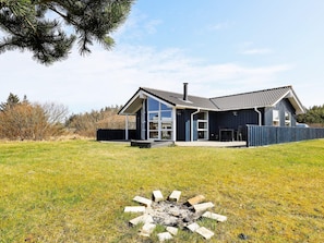 A modern two-story house with a large deck, a chimney, and a fenced yard.