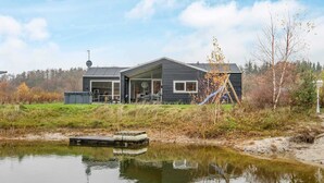 A modern house with a large glass door, a slide, and a dock by a pond.
