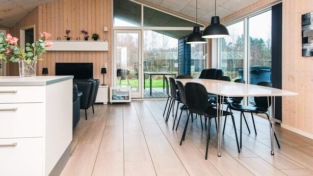 A modern kitchen with a large island, wooden walls, and a dining area with a table and chairs.