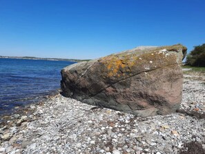 A large rock by a pebbly shore with clear blue water and a distant shoreline. - 5 Star Holiday Home in Sydals (Sydals)
