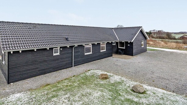 Een gebouw met twee verdiepingen, een donkere gevel, een grindpad en een gazon ervoor.