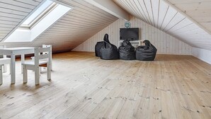 Een kamer met een schuine kap, dakraam, televisie en een witte stoel.