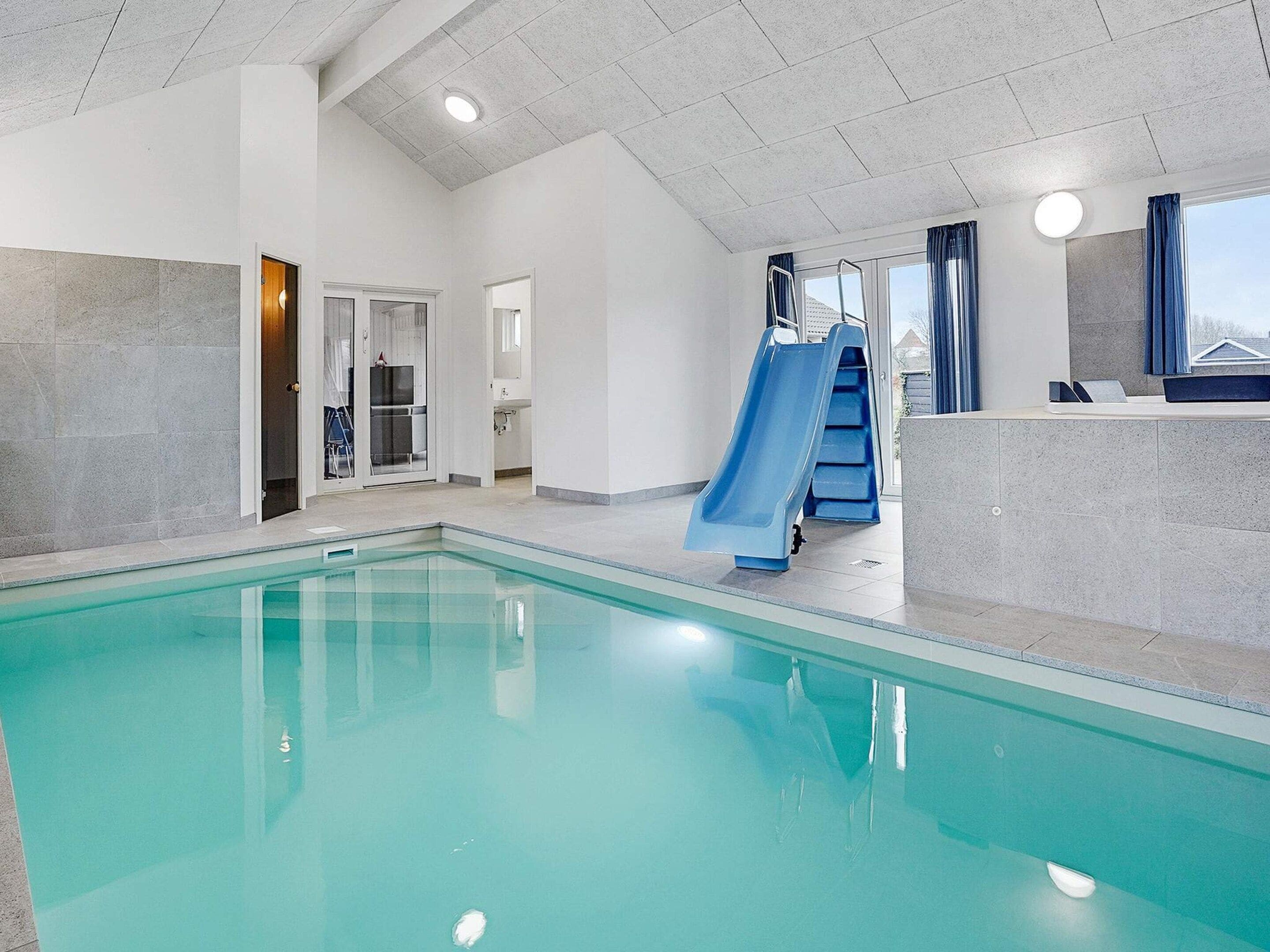 Ein Hallenbad mit Rutsche, einer Rezeption und Blick ins Freie.