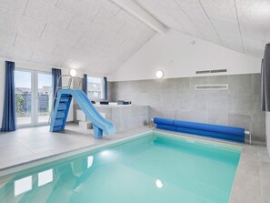 An indoor swimming pool with a blue slide, a seating area, and a reception desk.