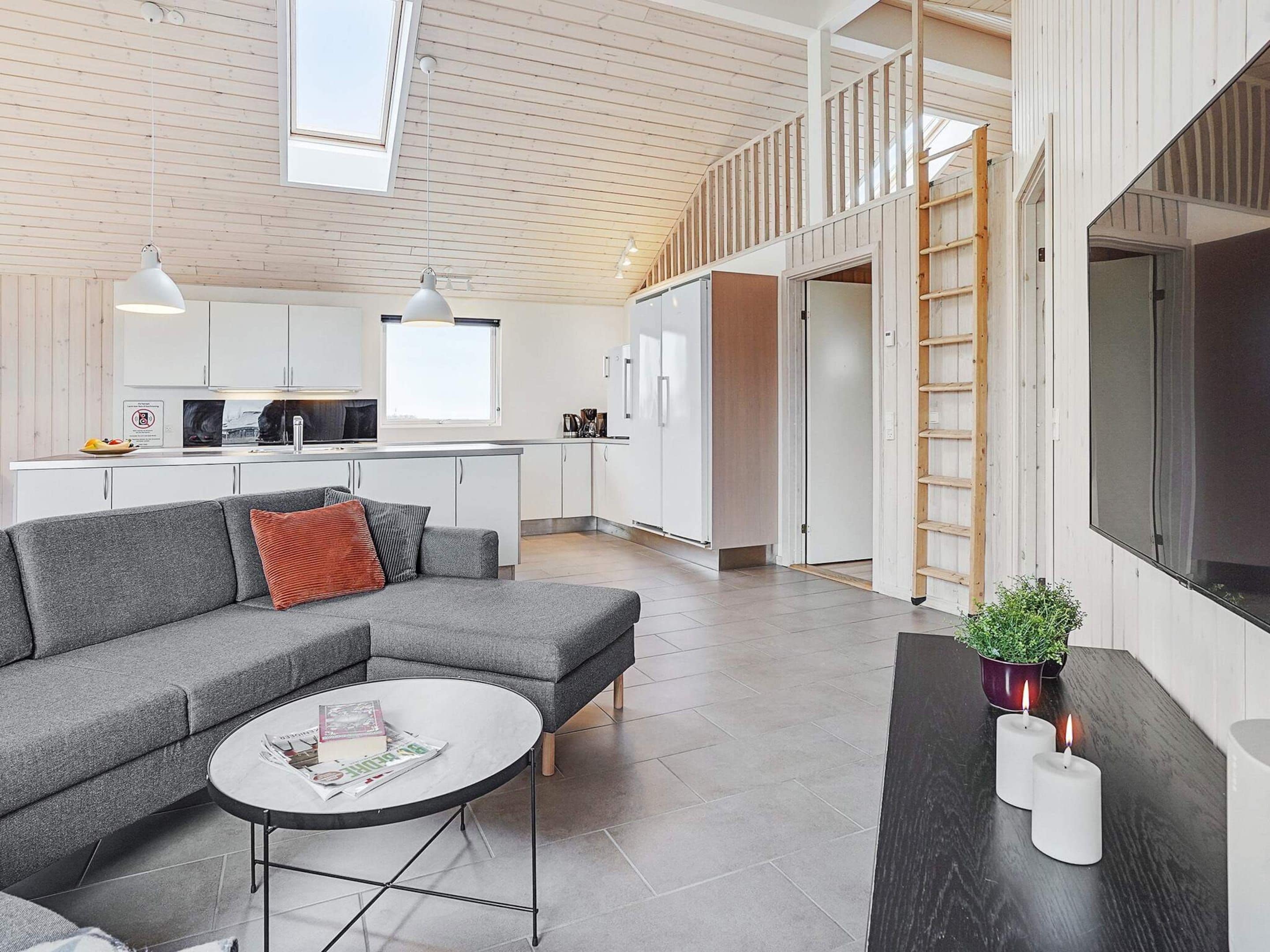 A modern interior with a grey sofa, a round coffee table, and a kitchen area with white cabinets and a wooden ceiling.