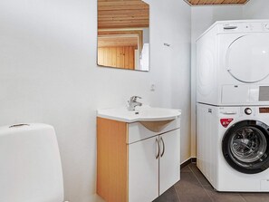 A compact, modern bathroom with a built-in washing machine, a sink, and a mirror.