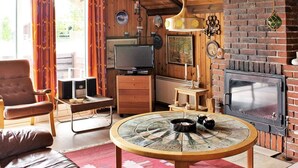 A cozy living room with a wooden ceiling, a brick fireplace, a television, and a round table with candles. - 6 Person Holiday Home in Vejers Strand-by Traum (Vejers Strand)