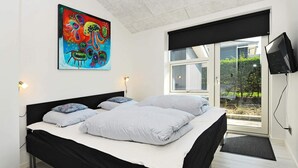 A modern bedroom with a large bed, a colorful abstract painting, a television, and a view of greenery outside. - Seaside Bliss in Fyn - By Traum Ferienwohnungen (Faaborg)