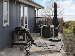 A patio with a grill, a table with chairs, and an umbrella. - Seaside Bliss in Fyn - By Traum Ferienwohnungen (Faaborg)