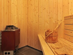 A wooden sauna room with a sauna bench, a wooden bucket, and a sauna heater. - Seaside Bliss in Fyn - By Traum Ferienwohnungen (Faaborg)