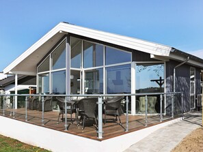A modern house with large glass windows, a covered patio with wicker furniture, and a clear blue sky. - Seaside Bliss in Fyn - By Traum Ferienwohnungen (Faaborg)