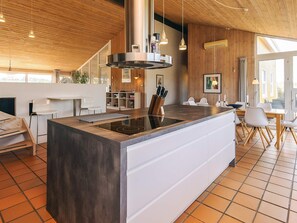 A modern kitchen with a central island, wooden ceiling, and a dining area with chairs and a table. - 4 Star Holiday Home in Hjorring (Hjørring)