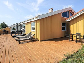 Une terrasse en bois avec des chaises longues et un barbecue.