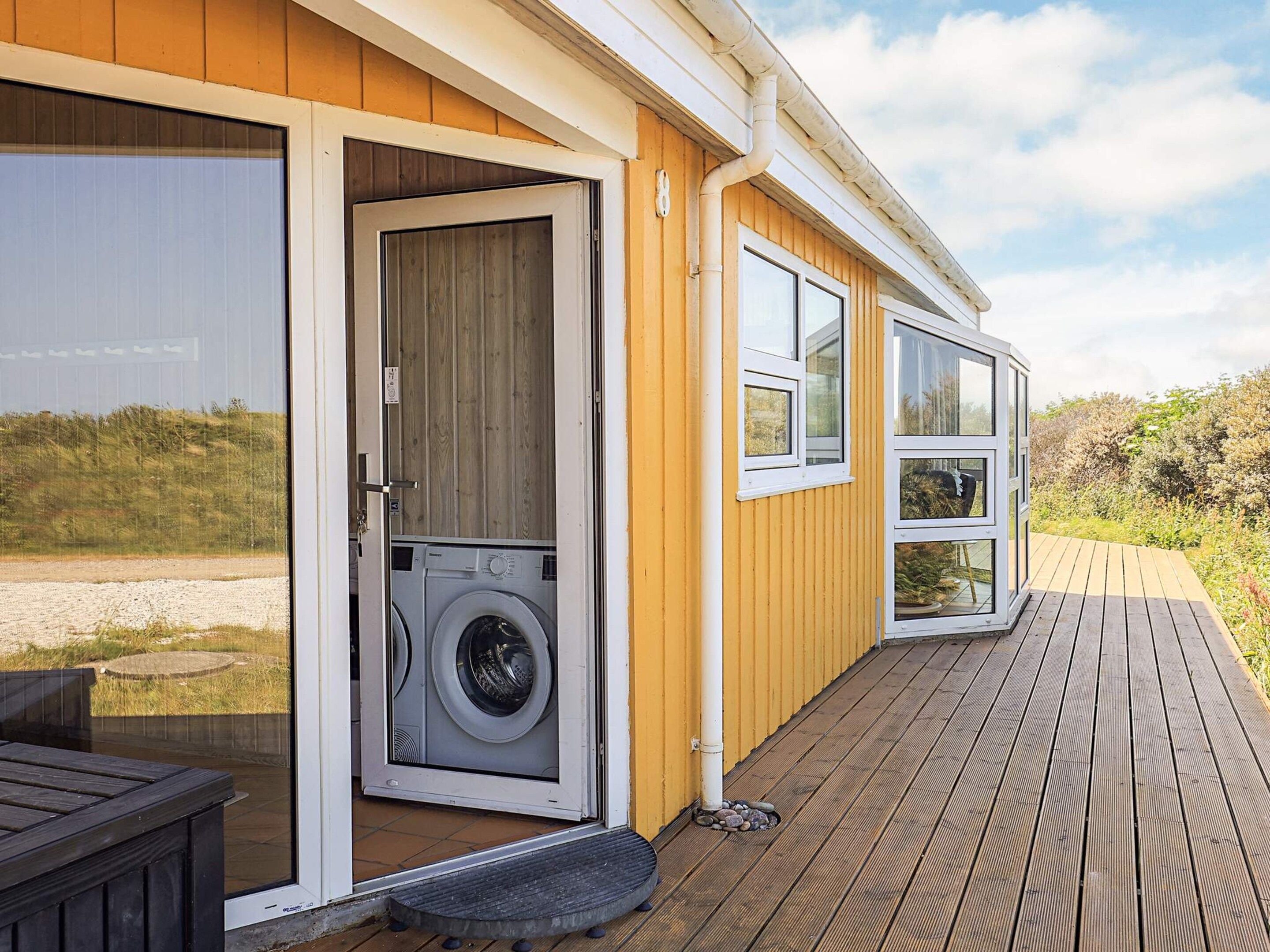 A wooden exterior with a door leading to a laundry area, a deck, and a view of the surrounding landscape.