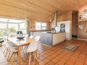 A modern kitchen with a central island, white cabinetry, and a dining area with a wooden table and chairs. - 4 Star Holiday Home in Hjorring (Hjørring)