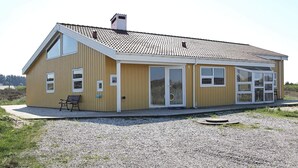 A yellow building with a tiled roof, large windows, and a bench outside. - 4 Star Holiday Home in Hjorring (Hjørring)