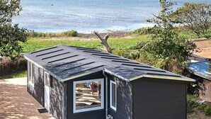 Uma estrutura moderna e escura ao ar livre, com telhado inclinado, porta de vidro e vista para o mar.