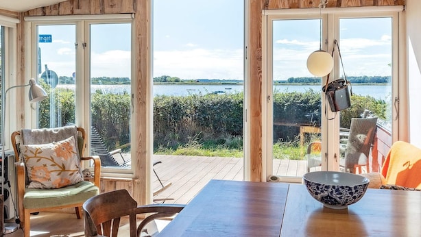 Quarto com deck de madeira, mesa de jantar e vista para um lago.