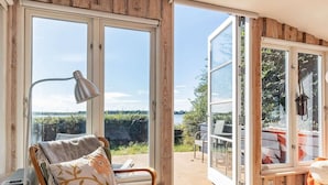 Um quarto acolhedor com vista para um lago, uma poltrona com almofada, uma luminária e uma mesa com cadeiras.
